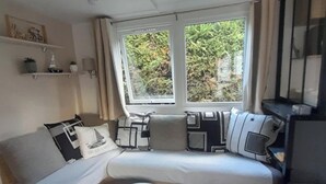Ein gemütliches Wohnzimmer mit einer Couch, zwei kleinen Tischen und einem Fenster mit Blick auf Grünflächen.