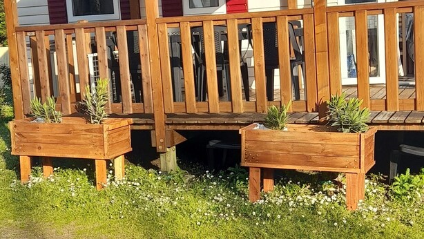 Eine Holzterrasse mit Geländer, zwei Pflanzgefäße aus Holz mit Pflanzen und einem strahlend blauen Himmel.