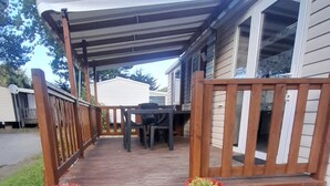 Eine überdachte Terrasse im Freien mit Holzgeländer, einem Picknicktisch und zwei Blumentöpfen.