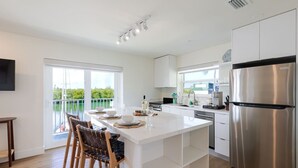 A modern kitchen with a large island, stainless steel appliances, and a view of a balcony with greenery. - Boot Key Harbor Retreat with Pool & Breakfast (Marathon)
