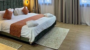 Ein Hotelzimmer mit einem großen Bett, einem Kopfteil, einem Nachttisch, einer Wandleuchte und einem Fenster mit Vorhängen.