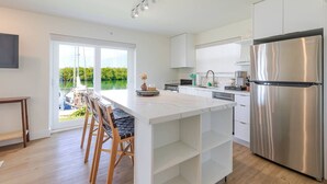 Une cuisine moderne dotée d’un grand îlot central, d’appareils électroménagers en acier inoxydable et offrant une vue sur un plan d’eau.