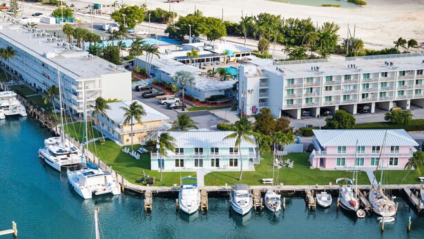 Un port de plaisance où sont amarr és de nombreux bateaux, un hôtel avec une piscine et, au loin, une plage.