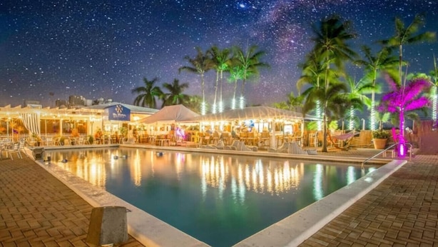 Ein Poolbereich bei Nacht mit freier Sicht auf den Pool, Liegestühle und Palmen.
