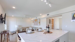 Eine moderne Küche mit einer großen Kochinsel, ein Essbereich mit einer Couch und ein Wohnzimmer mit Fernseher.