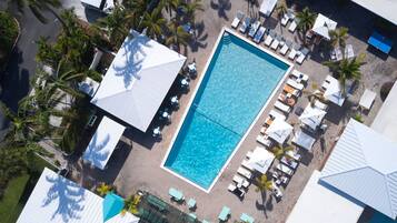 An aerial view of a resort with a central swimming pool, sun loungers, and palm trees.