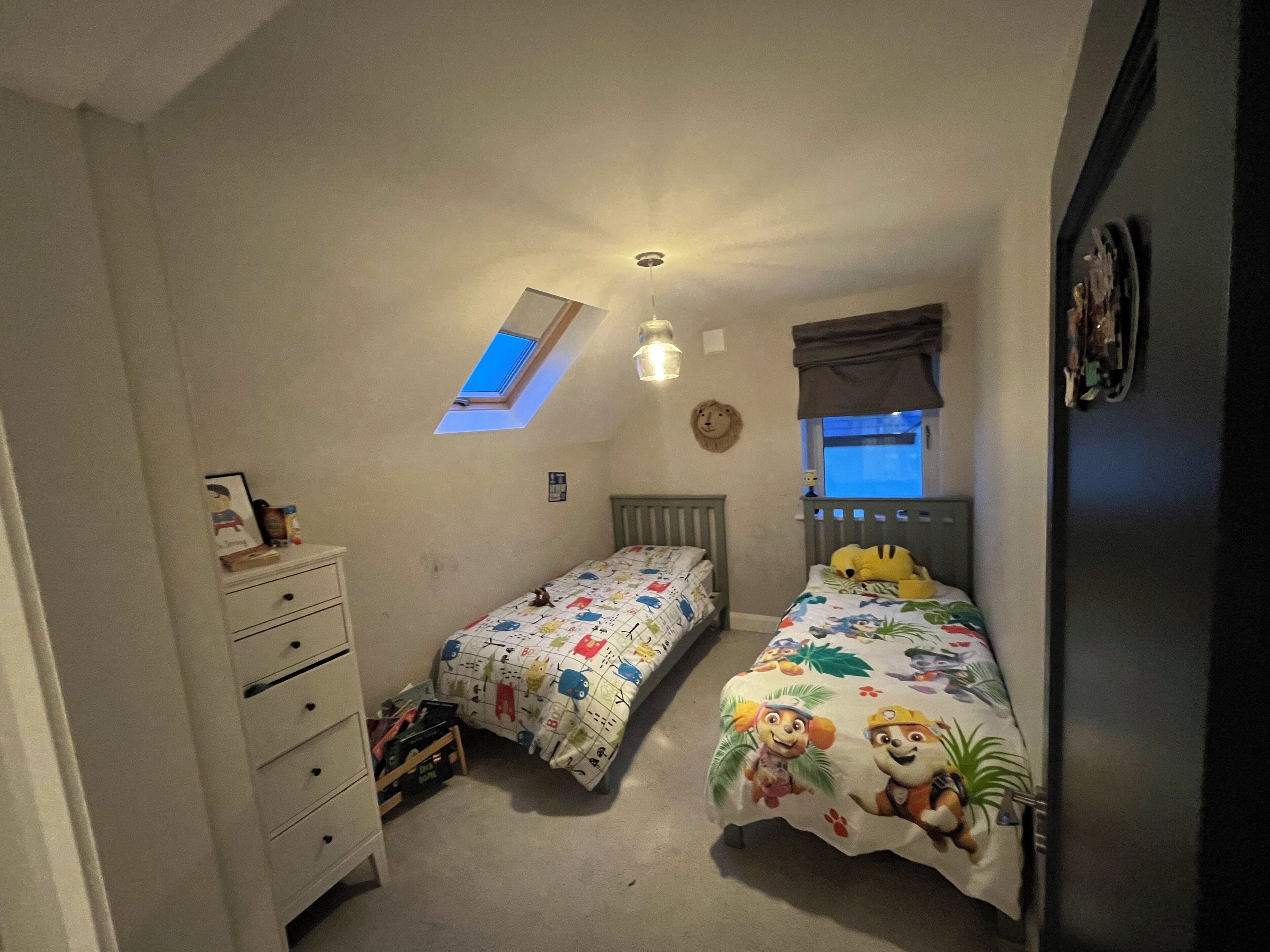 A small bedroom with two beds, a dresser, a skylight, and a window.