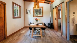 Un comedor con una mesa y sillas de madera, una lámpara colgante y un cuadro en la pared.