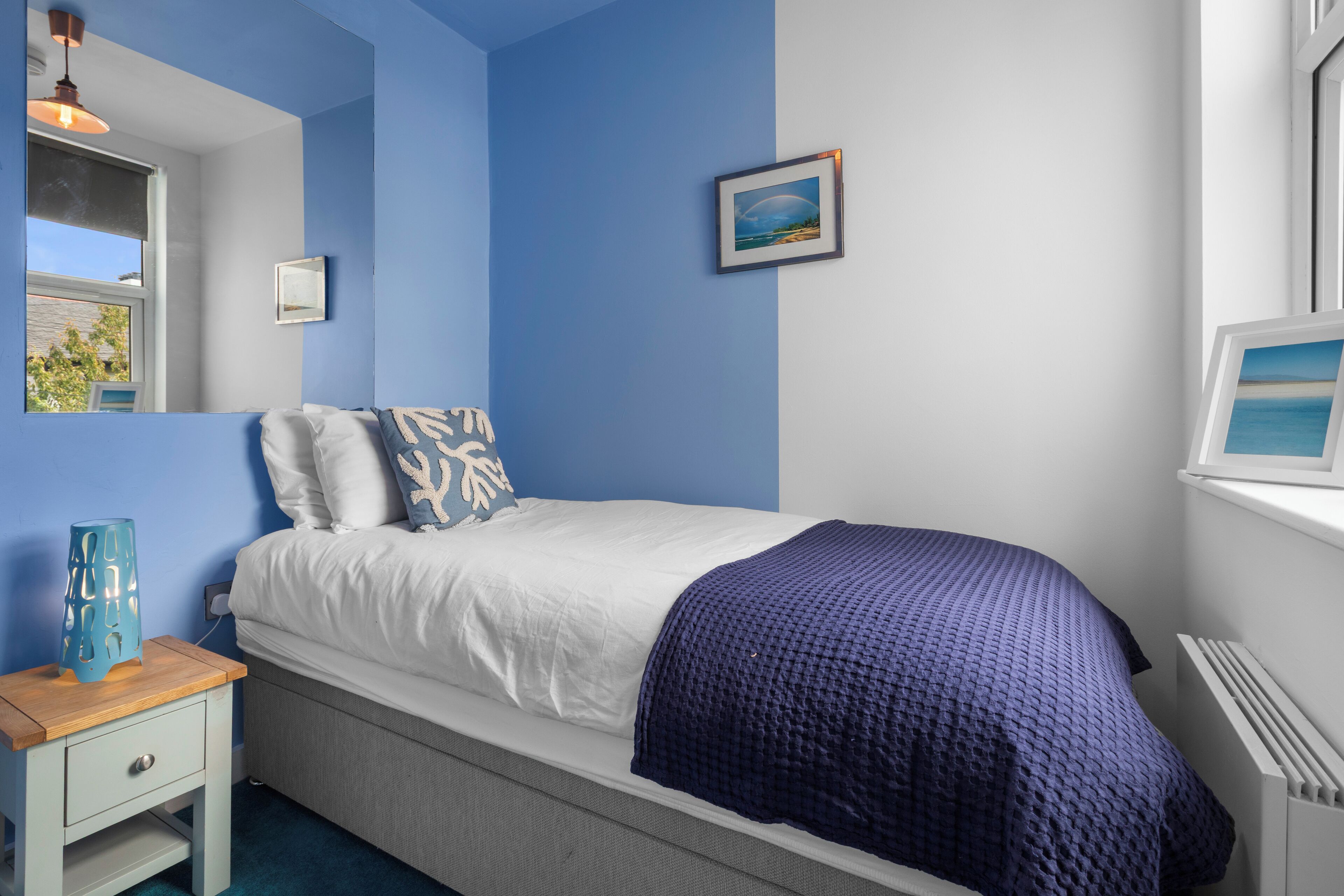 A bedroom with a bed, a nightstand, a window with a view, and a wall-mounted picture.