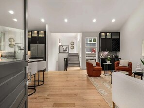 A modern kitchen with dark cabinets, a dining area with white chairs, and a staircase leading to a loft bedroom. - Germantown Gem! Skyline Views | 6 mins to Broadway (Nashville)