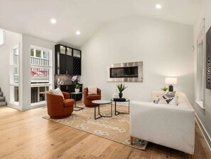 A modern living room with a fireplace, a flat-screen TV, and a dining area with a kitchen in the background. - Germantown Gem! Skyline Views | 6 mins to Broadway (Nashville)