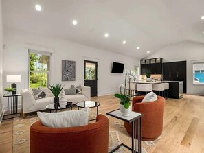A spacious living area with a sofa, ottoman, and coffee table, a kitchen with black cabinets, and a dining area with a bar. - Germantown Gem! Skyline Views | 6 mins to Broadway (Nashville)