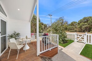 A covered outdoor patio with a dining table and chairs, a barbecue grill, and a white fence. - AquaLuna Beach House (Aireys Inlet)