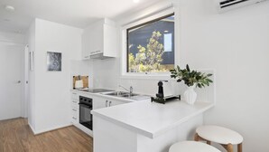 Moderni keittiö, jossa on valkoiset kaapit, sisäänrakennettu uuni, pesuallas ja ikkuna, josta avautuu näkymä puuhun.