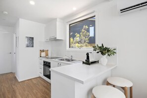 A modern kitchen with white cabinetry, a built-in oven, a sink, and a window overlooking a tree.