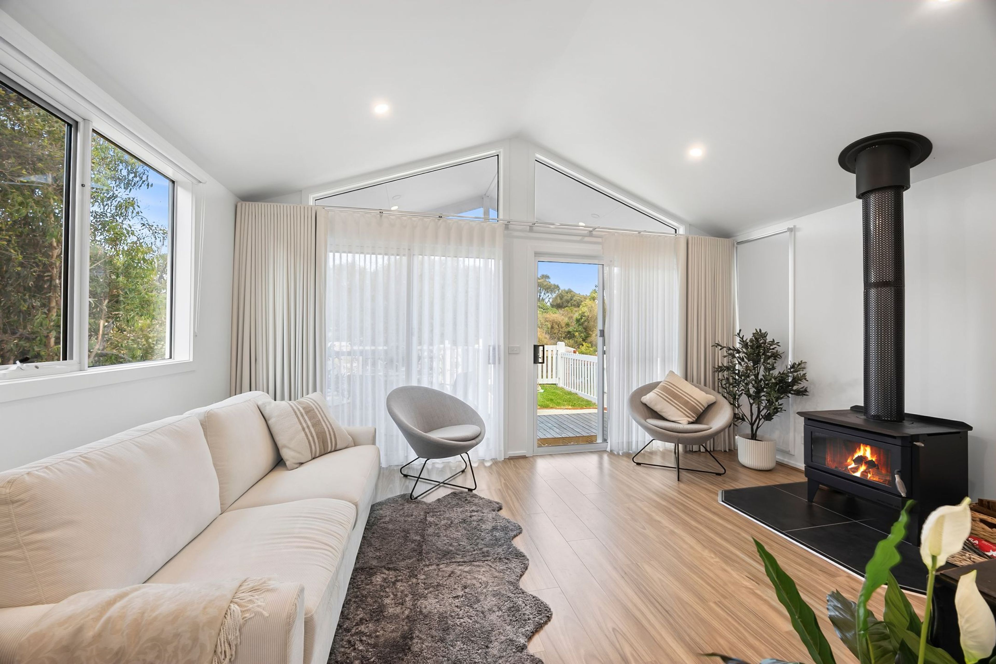 A modern living room with a sofa, chairs, a fireplace, and a view through a glass door.