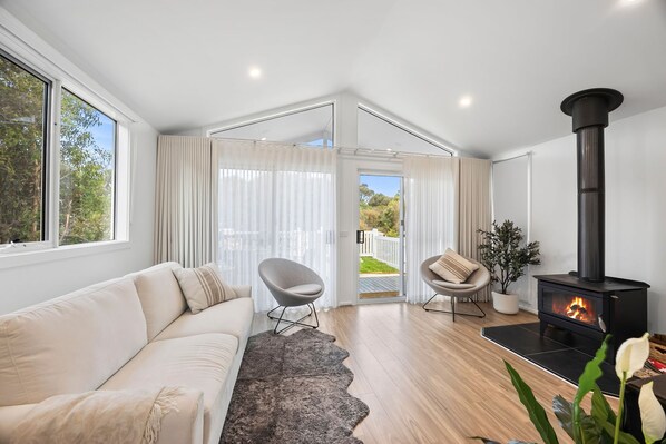 A modern living room with a sofa, chairs, a fireplace, and a view through a glass door.