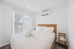 A hotel room with a large bed, a wooden headboard, a bedside table with a telephone, and a window with a view of the outside. - AquaLuna Beach House (Aireys Inlet)