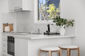 A modern kitchen with a white countertop, a built-in oven, a sink, and two bar stools.