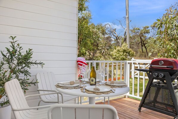 A deck with a table set for two, a grill, and a chair.