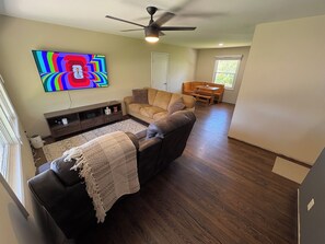 Una sala de estar con un sofá, un televisor, un ventilador de techo y una mesa de comedor de madera.