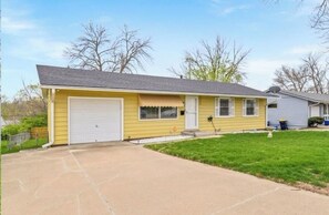 A single-story yellow house with a garage, a front yard, and a clear sky.