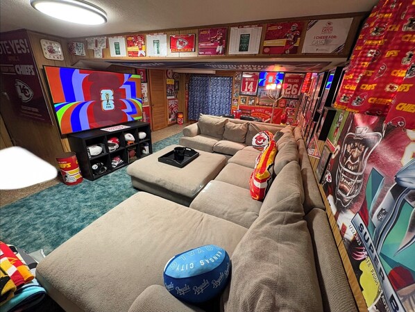 Una sala de estar con un televisor grande, un sofá modular y varios recuerdos deportivos.