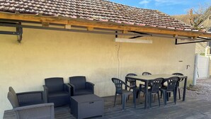 An outdoor patio with wicker furniture, a table, and chairs. - Gîte Les Rondières (Pougny)