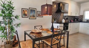 A modern kitchen with a glass dining table, black chairs, a hanging light fixture, and a bamboo plant. - Sea view-Town-House-Comfort-Private Bathroom (Nerja)