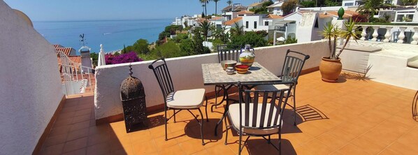 A terrace with a table and chairs, a potted plant, and a view of the sea and buildings. - Sea view-Town-House-Comfort-Private Bathroom (Nerja)