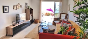 Ein modernes Wohnzimmer mit Fernseher, Sofa, Couchtisch und Blick ins Freie.