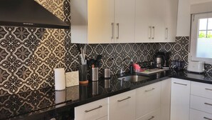 Een keuken met een betegelde achterwand, witte kasten en een zwart aanrecht.
