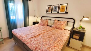 Een slaapkamer met een bed, nachtkastje, spiegel en raam met gordijnen.