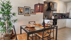 Een moderne keuken met een glazen eettafel, zwarte stoelen, een hanglamp en een bamboe plant.