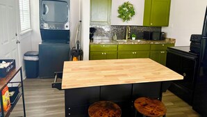 Cocina pequeña con armarios verdes, encimera de madera y dos taburetes.