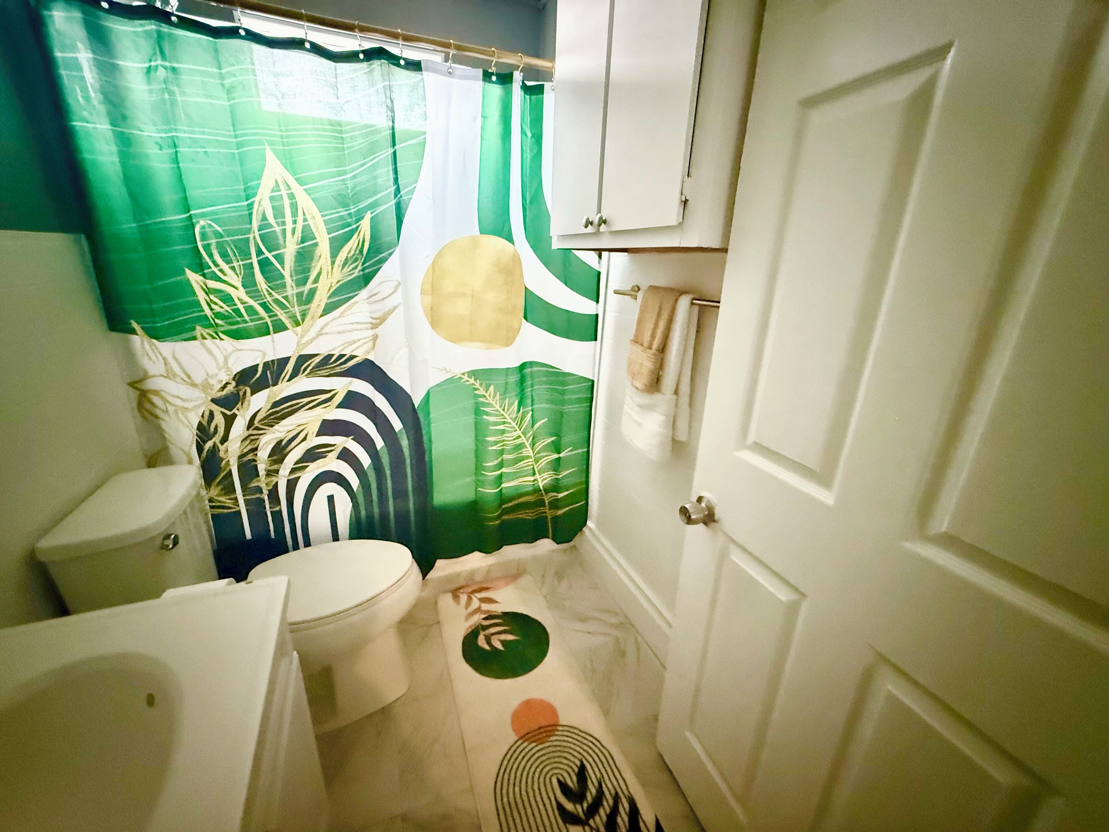 Ein kleines Badezimmer mit Toilette, Waschbecken und einer Duschvorhang mit Blättermuster.