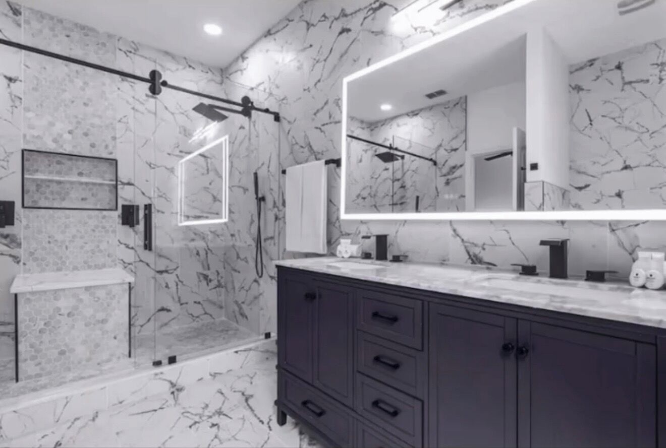 A modern bathroom with a marble backsplash, a large mirror, a dark vanity, and a shower area.