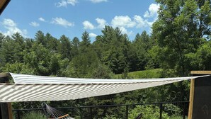 A deck with a hammock, two wicker chairs, and a wooden floor.