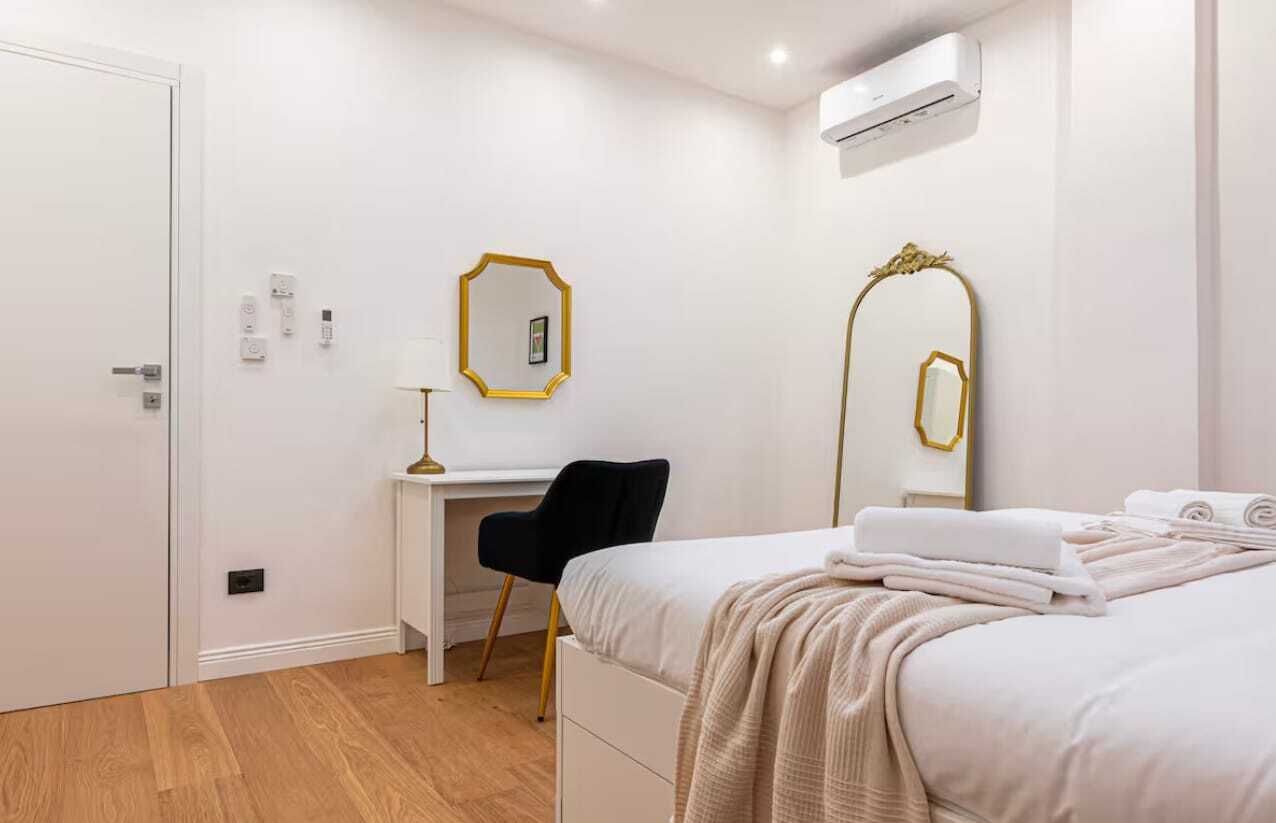 A bedroom with a bed, a desk, a chair, and a mirror.