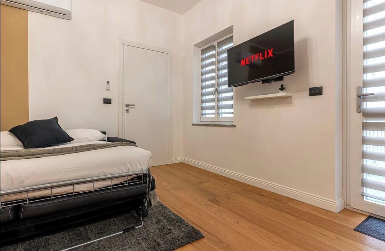 Une chambre à coucher avec un lit, un téléviseur fixé au mur et une fenêtre avec des stores.