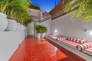 A narrow corridor with red tiled flooring, white walls, and a seating area with striped cushions. - Luxury 4 BR House Inside The Walled City With Maid And Staff (cartagena)