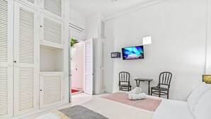 Et hotelværelse med seng, fjernsyn, to stole og en garderobe med åbne døre.