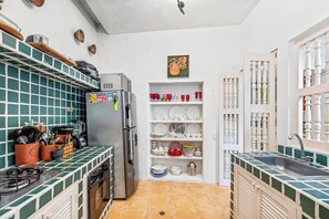 Eine kleine Küche mit Kühlschrank, Herd und Regalen mit Geschirr.