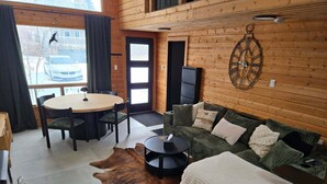 Interior acogedor de una cabaña con paredes de madera, una mesa redonda para comer, un sofá y una alfombra de cuero.