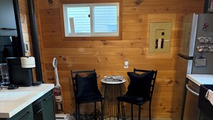 Una cocina compacta con paredes de madera, una pequeña mesa de comedor con dos sillas, un refrigerador y una cafetera.