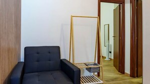 Et værelse med en mørk sofa, trægulv og en gang der fører til en dør.