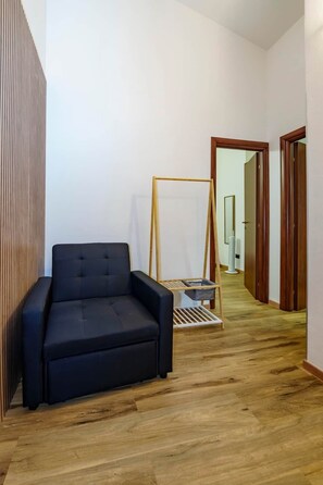 Una habitación con un sofá oscuro, piso de madera y un pasillo que conduce a una puerta.