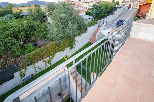 A residential area with a balcony, a green lawn, and a road with a parked car.