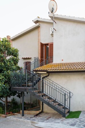 A residential building with a staircase leading to a balcony, a satellite dish, and a small garden area.