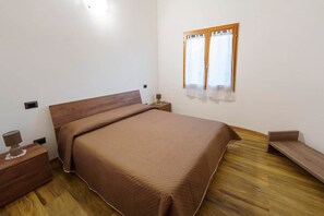 Un dormitorio con una cama de madera, una mesita de noche con lámpara y una ventana con cortinas.